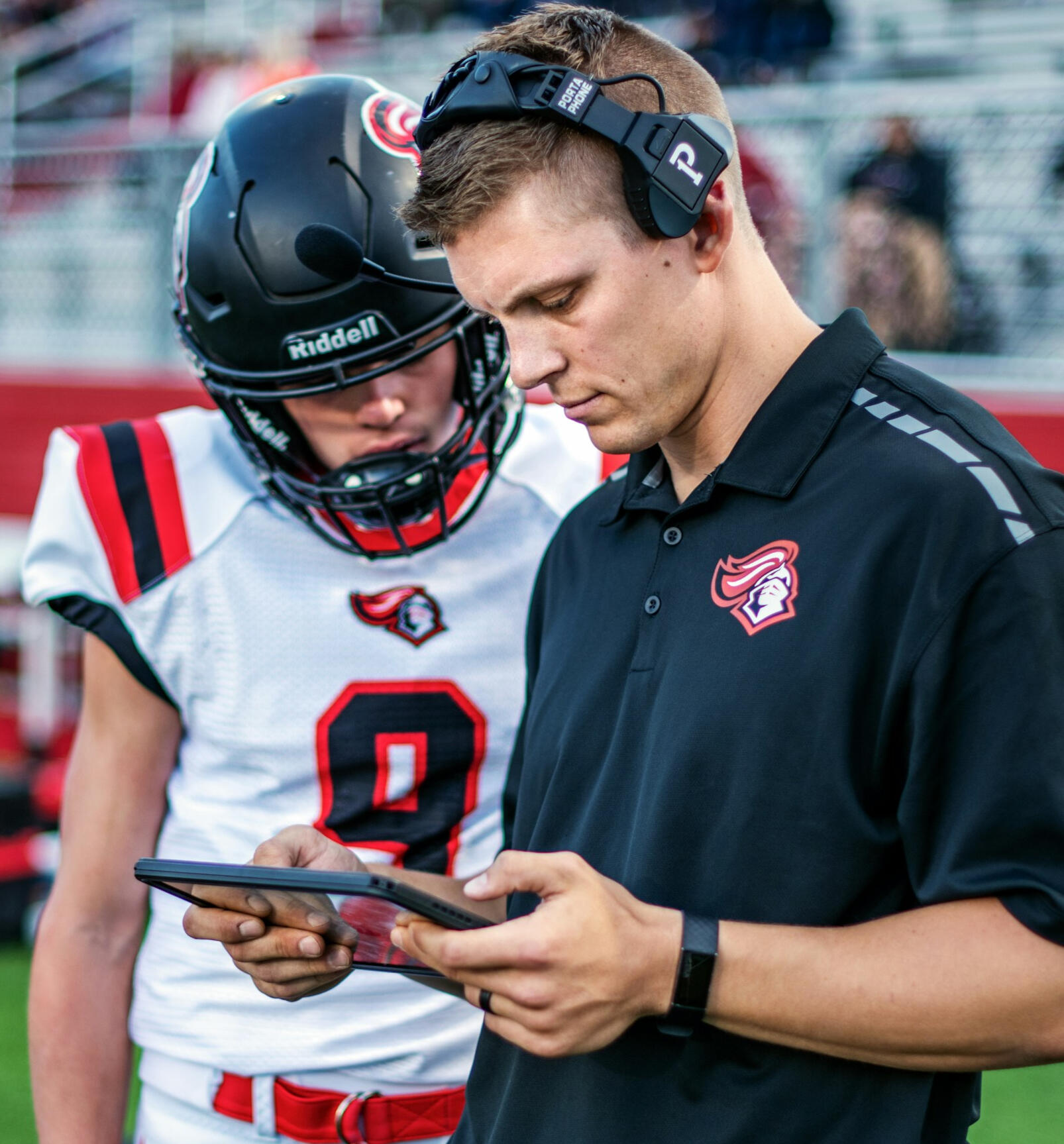 Entrenador de fútbol americano mostrando tácticas en una tablet a un jugador, destacando aprendizaje en tiempo real y entrenamiento mental situacional.