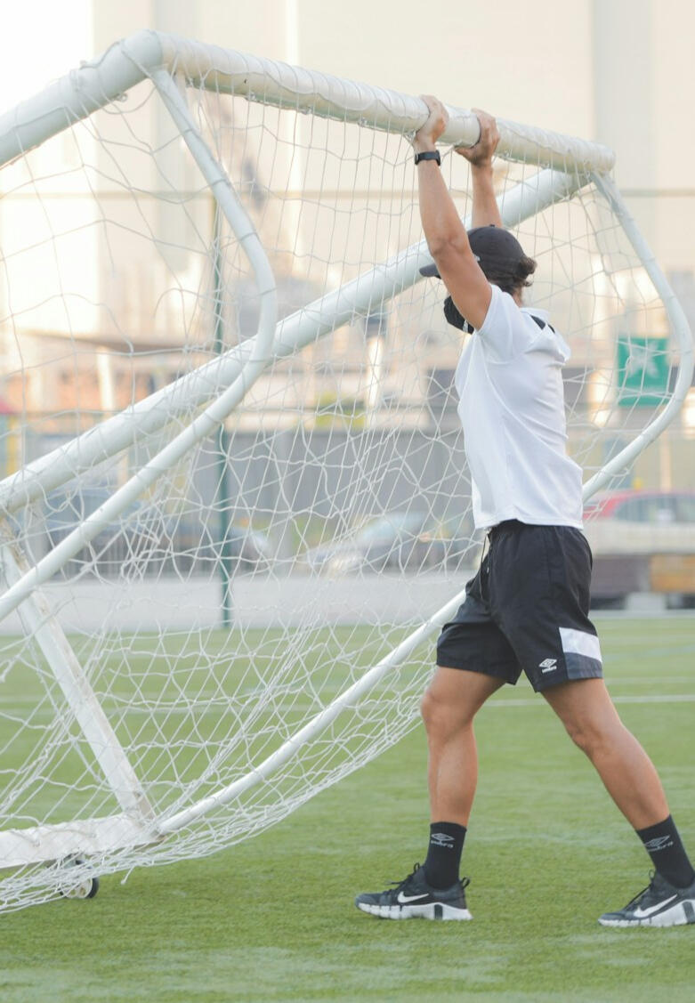 Entrenador de fútbol desplazando una portería móvil en el campo, simbolizando liderazgo desde el ejemplo y compromiso con su equipo.