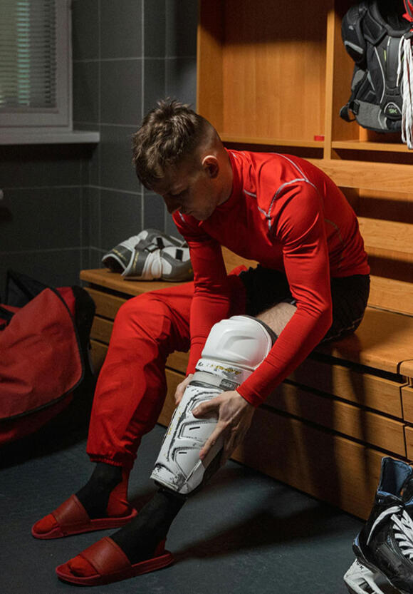 Jugador de hockey hielo en el vestuario poniéndose las espinilleras, simbolizando preparación, ritual y mentalidad previa al partido.