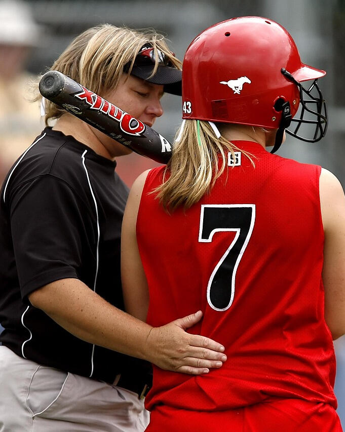Entrenadora de softball femenino hablando con una jugadora, fomentando confianza, desarrollo y resiliencia emocional.