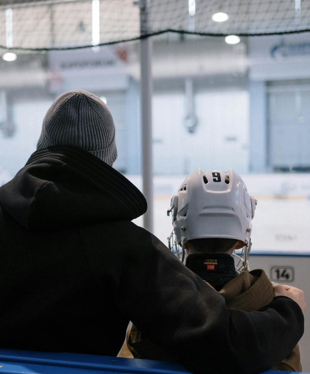 Padre e hijo viendo un partido de hockey hielo juntos, simbolizando apoyo familiar, desarrollo deportivo a largo plazo y raíces emocionales.